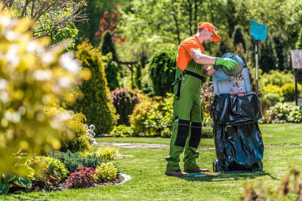 Caucasian gardener working in the green garden and cleaning it from leaves and grass
